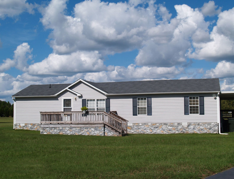 Gray trailer home with stone foundation or skirting and shutters in front of a beautiful sky.